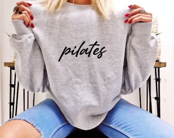 May include: A gray sweatshirt with the word "pilates" written in black cursive lettering.