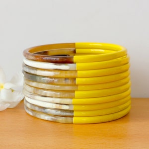 May include: A stack of yellow and brown bangles. The bangles are made of horn and are half painted yellow.