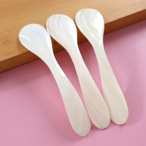 May include: Three white mother of pearl spoons with a rounded bowl and a long, slender handle.