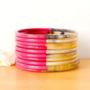 May include: A stack of pink and natural horn bangles. The bangles are half pink and half natural horn.