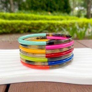 May include: A stack of colorful bracelets with a tortoiseshell pattern. The bracelets are made of a hard plastic material and have a glossy finish. The colors of the bracelets are turquoise, pink, yellow, red, green, blue, and orange.