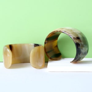 May include: Two brown and beige horn bracelets. The bracelets are made of natural horn and have a unique, organic pattern.