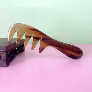 May include: A brown tortoiseshell comb with a wide handle and five teeth. The comb is lying on a pink surface.
