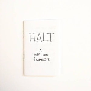 May include: A white booklet with the text "HALT. A self-care framework" written in black ink.
