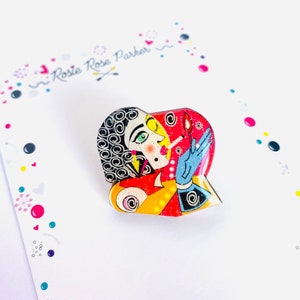 Peut inclure: Une épingle en forme de cœur avec une illustration colorée d'une femme avec une cigarette à la bouche. L'épingle est en métal et a une finition brillante.
