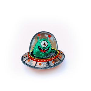 Peut inclure: Épinglette fantaisiste représentant un extraterrestre vert à un œil avec un large sourire à l'intérieur d'un OVNI argenté et rouge. L'extraterrestre a des antennes rouges et est placé dans un dôme transparent.