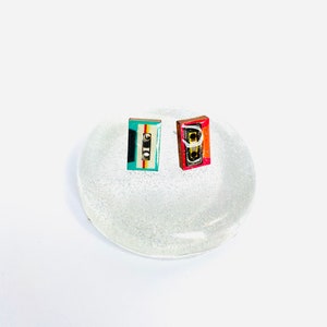 May include: Two small cassette tape earrings, one is red, white, and blue, the other is teal, white, and black.