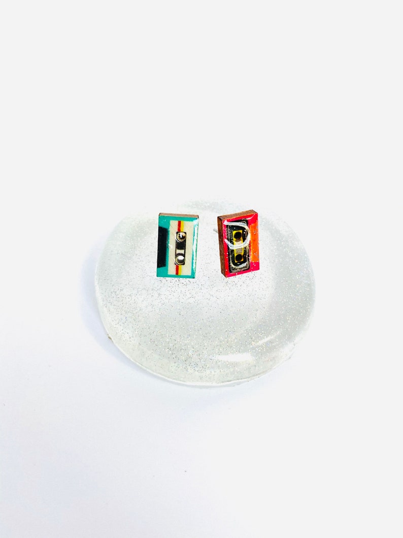 May include: Two small cassette tape earrings, one is red, white, and blue, the other is teal, white, and black.