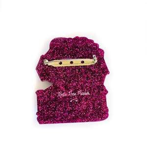 May include: A pink glitter pin with a rose design and the text "Rosie Rose Parker" in white.