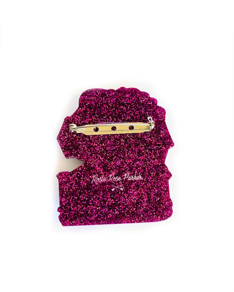 May include: A pink glitter pin with a rose design and the text "Rosie Rose Parker" in white.