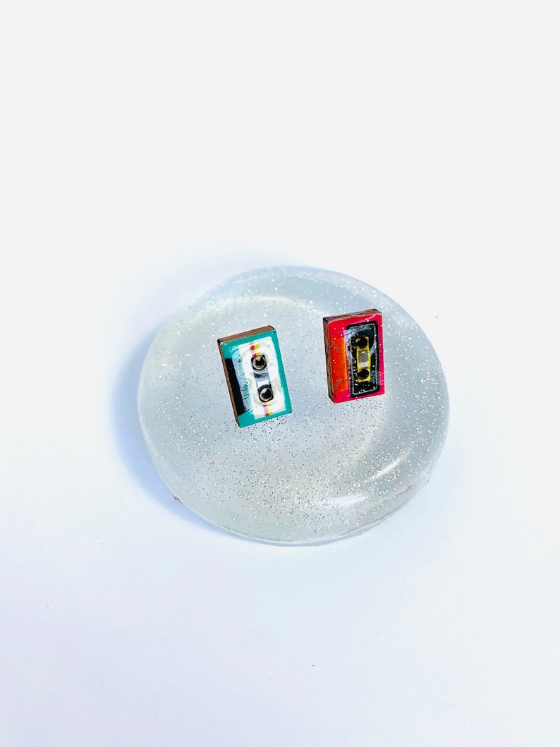 May include: A pair of small cassette tape earrings. One earring is red, black, and white. The other earring is teal, black, and white.