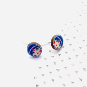 May include: A pair of wooden earrings with a blue and white design featuring a cartoon face with pink cheeks and a red dot on the forehead.
