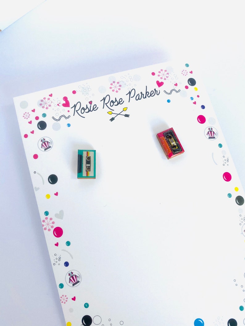 May include: A pair of small, colorful cassette tape earrings. The earrings are on a white card with the text "Rosie Rose Parker" and a heart design.