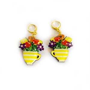 May include: A pair of gold hoop earrings with a yellow and white striped teacup design. The teacup is filled with colorful flowers.