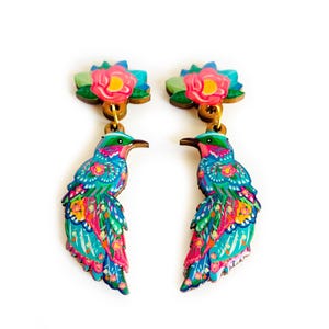 May include: A pair of colorful wooden earrings featuring a bird with a floral design and a pink flower on top.