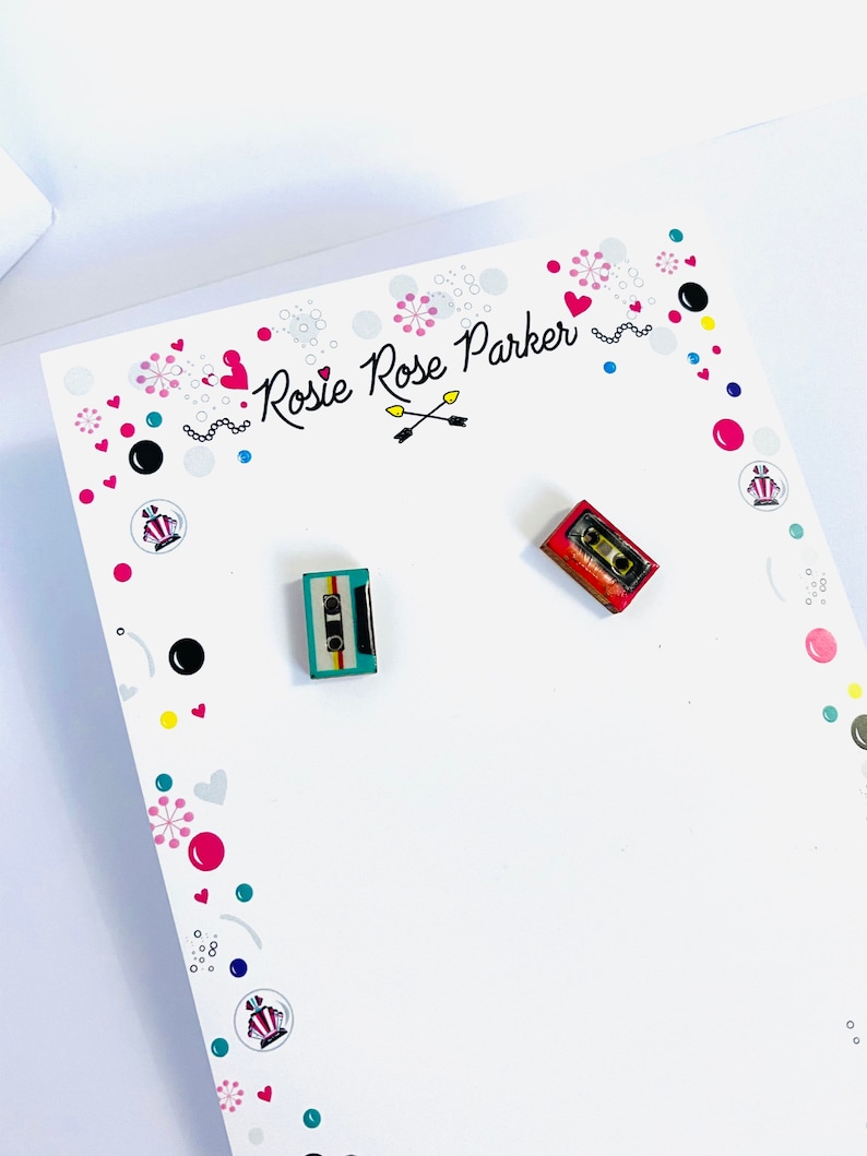 May include: A white card with the text "Rosie Rose Parker" and a pair of cassette tape earrings. One earring is red and the other is blue and green.