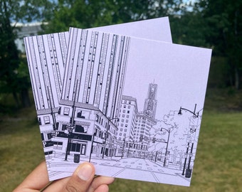 May include: A black and white line drawing of a city street scene with tall buildings, a street sign that says "One Way", and a street lamp. The drawing is on a white card.
