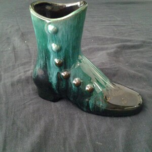 May include: A green ceramic boot-shaped vase with black accents and gold-coloured buttons. The vase has a glazed finish.