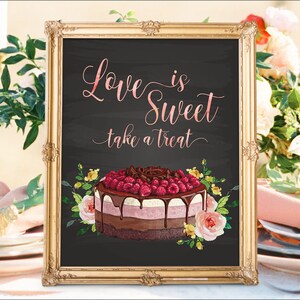 May include: A framed chalkboard sign with gold trim. The sign reads "Love is Sweet take a treat" in pink script. A watercolor cake with raspberries and chocolate sits below the text, surrounded by flowers. The sign is likely for a wedding or party.