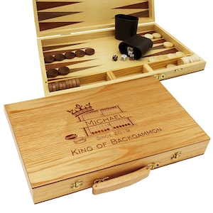 May include: A wooden backgammon set with a personalized inscription. The inscription reads "Michael Since 2019 King of Backgammon". The set is closed and has a wooden handle.
