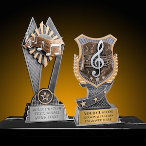 May include: Two music-themed trophies with silver, gold, and bronze accents. One trophy features a star and the text "YOUR CUSTOM TEXT, NAME, YOUR LOGO." The other trophy has a treble clef and the text "YOUR CUSTOM PERSONALIZATION ENGRAVED HERE."