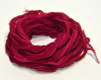 May include: A spool of deep crimson red silk ribbon, the ribbon is loosely wound and has a slightly textured surface.