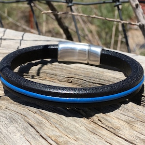 May include: A black leather bracelet with a thin blue stripe and a silver magnetic clasp.