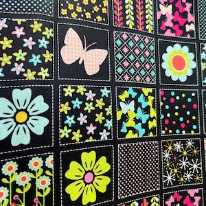 May include: A black fabric with a patchwork design featuring various floral and butterfly patterns. Each square has a different design, including flowers, butterflies, and polka dots in bright colors like pink, yellow, and blue. The squares are outlined with white stitching.