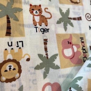 May include: White fabric with a repeating pattern of cartoon animals and palm trees. The animals include a tiger, lion, and elephant. The word "Tiger" is printed below the tiger illustration.