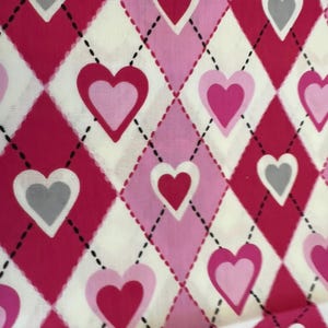 May include: Fabric with a repeating pattern of hearts and diamond shapes. The hearts are in shades of pink, with some having a gray center. The diamonds are in shades of pink and red, with a white background. Black dashed lines separate the diamonds.
