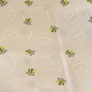 May include: Light gray fabric with a repeating pattern of yellow and black bees and white dotted lines. The bees are depicted in a cartoon style, and the lines form heart-shaped patterns.