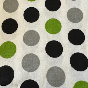 May include: Close-up of a white fabric with a repeating pattern of large polka dots. The dots are in three colors: black, gray, and lime green. The fabric has a slightly textured appearance.