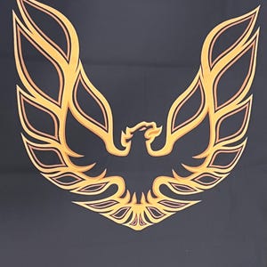 May include: A black background with a gold and orange stylized phoenix emblem. The emblem features a bird with outstretched wings, a classic design often associated with automotive branding.