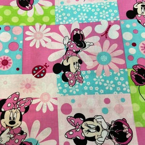 May include: A colorful fabric featuring Minnie Mouse in various poses, set against a patchwork of pink, green, and blue squares. The design includes white daisies, polka dots, and a ladybug, creating a cheerful and playful pattern.