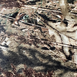 May include: Close-up of a camouflage pattern fabric. The design features a blend of brown, tan, and green hues, mimicking a forest environment. The fabric's texture appears slightly rough, with visible details of leaves and branches.