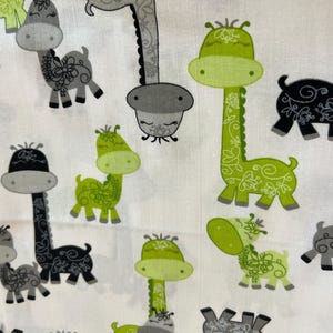 May include: White fabric with a repeating pattern of cartoon giraffes in shades of gray and green. The giraffes have floral designs and are in various poses. The overall design is whimsical and suitable for baby or children's products.