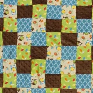 May include: A patchwork quilt featuring squares of various fabrics. The quilt includes squares of brown, light blue with a diamond pattern, and green with leaves. Other squares have owls and leaves.