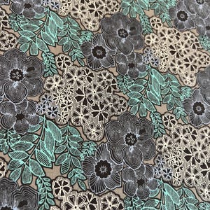 May include: A fabric with a floral pattern. The design features large, dark gray flowers with black centers, interspersed with smaller white and black floral clusters. Light teal leaves and stems are also present, all set against a tan background.