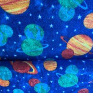 May include: Blue fabric with a repeating pattern of planets, stars, and rings. The planets are orange, yellow, green, and blue. White stars are scattered across the blue background.