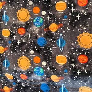 May include: A fabric with a repeating pattern of planets, stars, and the sun against a dark background. The planets are in shades of orange, blue, and yellow, with white stars and planet names. The sun is a bright orange circle.