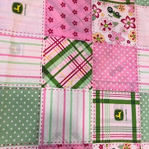 May include: A patchwork fabric with squares of pink, green, and white. The squares feature floral, polka dot, striped, and plaid patterns. Some squares have a John Deere logo and tractor graphic. The fabric is stitched together with a dashed line.