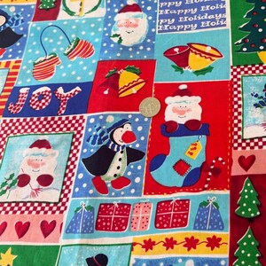 K&ouml;nnte beinhalten: Ein festlicher Baumwollstoff mit einem Patchwork-Muster aus Weihnachtsmotiven wie Schneem&auml;nnern, Pinguinen, Weihnachtsm&auml;nnern, Glocken, Geschenken und Herzen. Eine Silberm&uuml;nze mit 2,4 cm Durchmesser dient als Gr&ouml;&szlig;envergleich.
