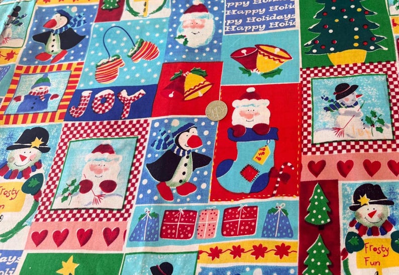 K&ouml;nnte beinhalten: Ein festlicher Baumwollstoff mit einem Patchwork-Muster aus Weihnachtsmotiven wie Schneem&auml;nnern, Pinguinen, Weihnachtsm&auml;nnern, Glocken, Geschenken und Herzen. Eine Silberm&uuml;nze mit 2,4 cm Durchmesser dient als Gr&ouml;&szlig;envergleich.