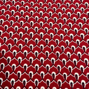 May include: Red fabric with a repeating pattern of white and black linked ovals. The design creates a textured, chain-like effect across the surface. The fabric is suitable for various sewing and crafting projects.