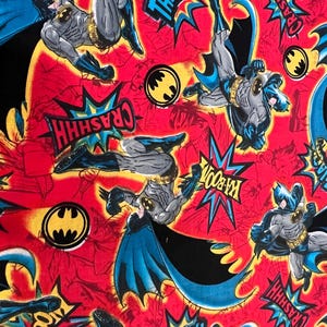 May include: Red fabric featuring multiple illustrations of Batman in action poses. Comic book style speech bubbles with words like "THACK" and "CRASSHH" are scattered throughout. The Batman logo is also visible.