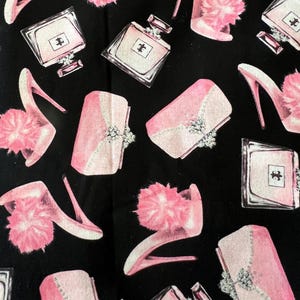May include: Black fabric with a repeating pattern of pink high heels with fluffy accents, perfume bottles, and clutch purses. The design features a glamorous, feminine aesthetic with a watercolor effect.
