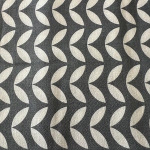 May include: Close-up of a fabric with a repeating pattern of white, leaf-shaped designs against a dark gray background. The leaves are arranged in vertical rows, creating a textured, geometric aesthetic.