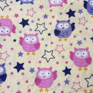 May include: A repeating pattern of owls and stars on a light yellow background. The owls are in shades of pink and purple, with yellow feet. Stars are in blue, pink, and outline form.