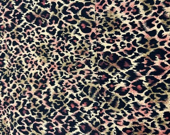 Könnte beinhalten: Nahaufnahme eines Stoffes mit Leopardenmuster. Das Design zeigt schwarze, braune und rosa Flecken auf beigem Hintergrund. Der Stoff scheint weich und flexibel zu sein, geeignet für Kleidung oder Accessoires.
