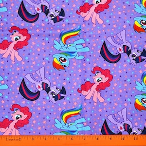 May include: A purple fabric featuring cartoon ponies in various poses, with pink, blue, and purple manes and tails. The background is covered in small stars in shades of pink, blue, and purple. A ruler is at the bottom.